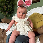 Vada joined the competition — help win amazing prizes! baby, child, bunny_ears, white_clothing, sitting, indoor, living_room, plant, green_wall, framed_picture, person, couch, carpet, cute, portrait, blue_eyes, plush, hands, legs, soft_lighting