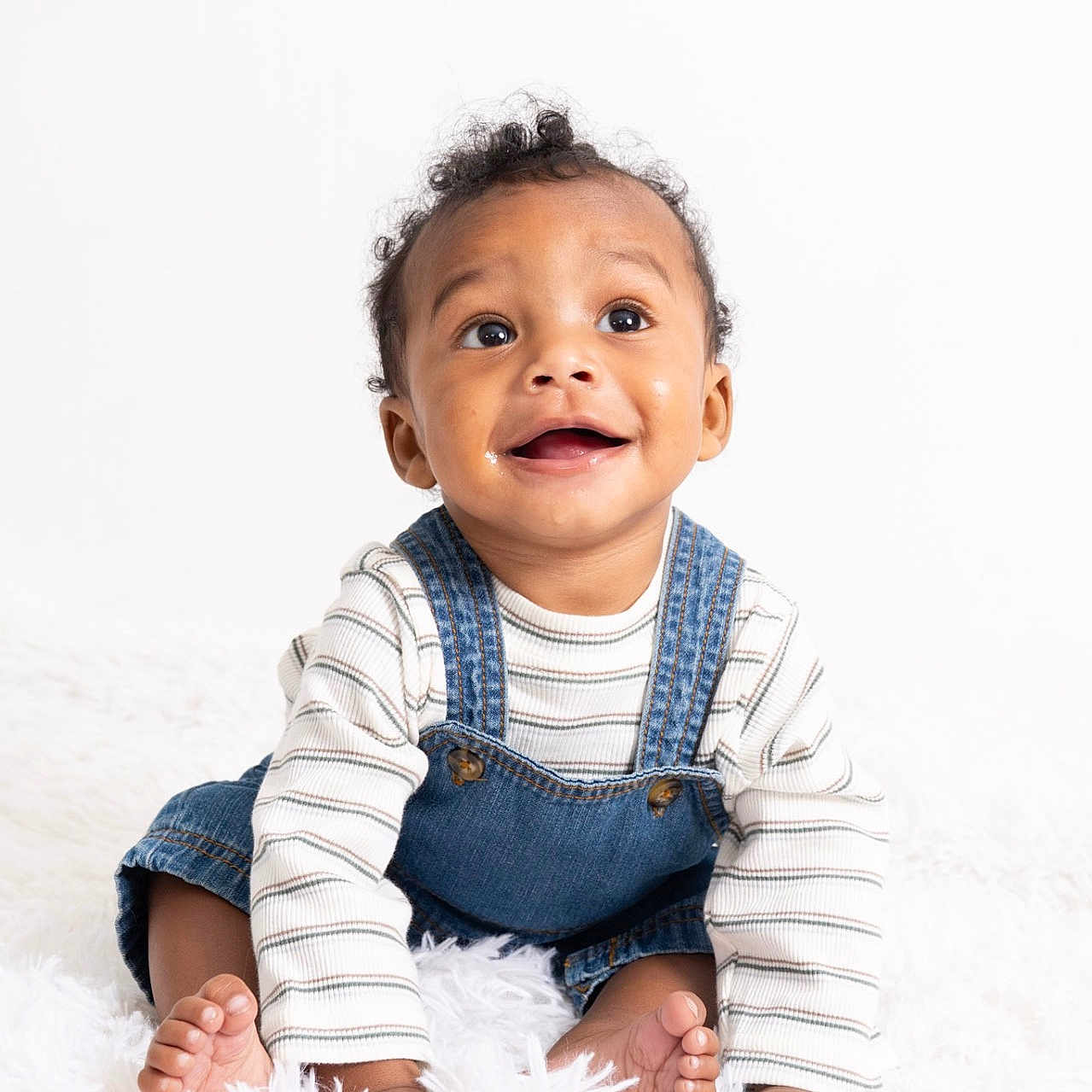 Khionyx joined the competition — help win amazing prizes! baby, barefoot, child, curly_hair, cute, denim_overalls, expression, face, fluffy_rug, happy, indoors, innocence, joy, portrait, sitting, skin, smile, striped_shirt, white_background, young_child