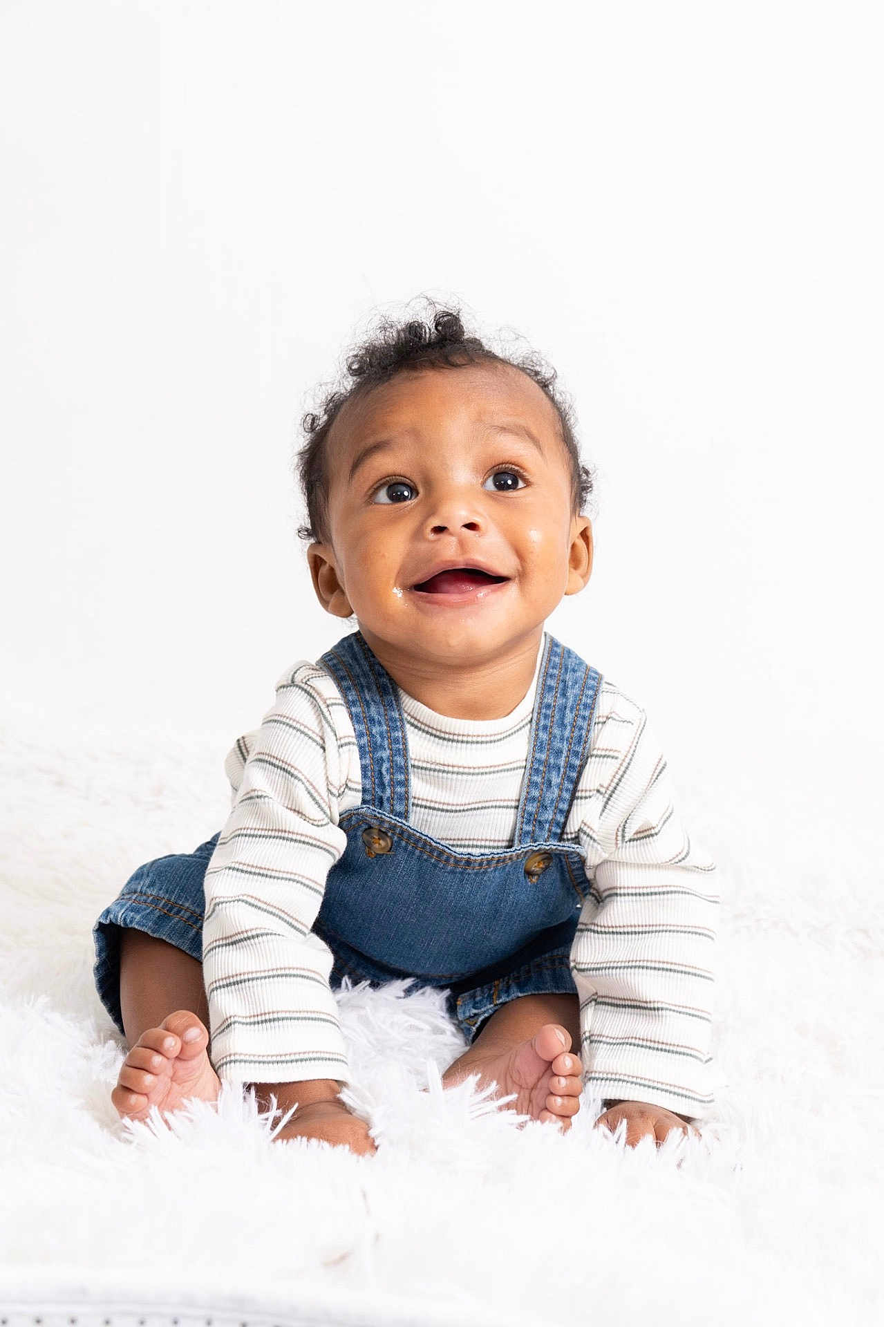 Khionyx joined the competition — help win amazing prizes! baby, child, smile, happy, denim_overalls, striped_shirt, curly_hair, sitting, white_background, fluffy_rug, cute, portrait, young_child, indoors, innocence, joy, expression, barefoot, skin, face