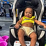 baby, baby_gear, car_seat, child, face, happy, indoor, infant, pink_basket, portrait, product_display, retail, seated, shopping, shorts, showroom, smiling, store, vehicle_safety, yellow_shirt