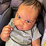 baby, infant, car_seat, grey_clothing, onesie, fist, face, eyes, head, person, child, seat_belt, fabric, pattern, closeup, indoor, expression, skin, hair, casual_wear