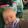 baby, infant, face, person, blanket, clothing, indoor, storage_bins, shelf, wood_floor, adult_arm, casual, resting, expression, closeup, head, skin, young_child, calm, household_items