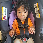 Mckenzie is registered to the contest to win money with this photo: baby, black_straps, car_seat, casual_clothing, child, curly_hair, cute, hands, indoor, infant, looking_up, orange_shirt, person, portrait, purple_padding, safety_harness, seat_belt, secured, warning_label, young_child
