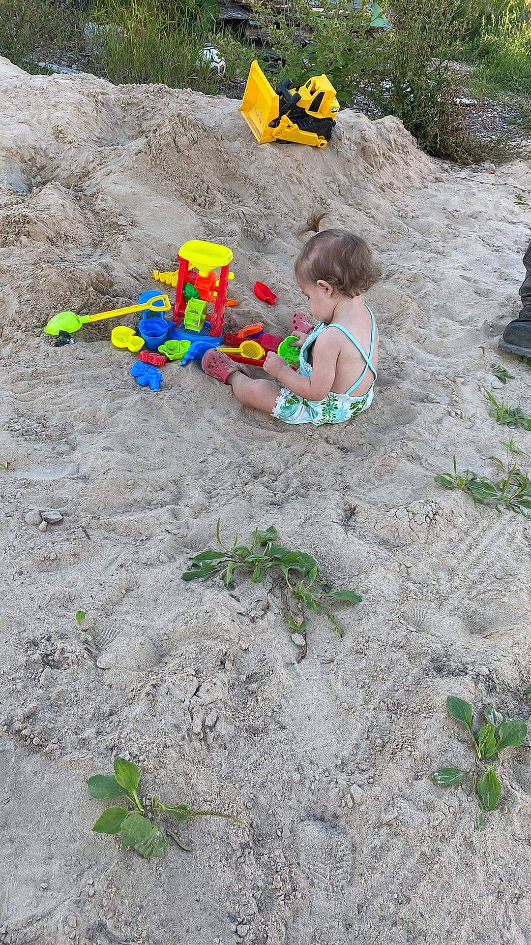 Gracelynn is registered to the contest to win money with this photo: child, fun, garden, grass, groundcover, landscape, leisure, people_in_nature, person, plant, plastic, play, recreation, rock, sand, sitting, soil, swimwear, toddler, toy