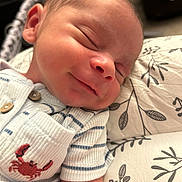 Elijah joined the competition — help win amazing prizes! newborn, baby, sleeping, smiling, onesie, striped_clothing, crab_embroidery, pillow, leaf_pattern, closeup, infant, face, head, peaceful, resting, soft_lighting, skin, cute, child, portrait