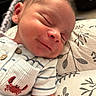 newborn, baby, sleeping, smiling, onesie, striped_clothing, crab_embroidery, pillow, leaf_pattern, closeup, infant, face, head, peaceful, resting, soft_lighting, skin, cute, child, portrait