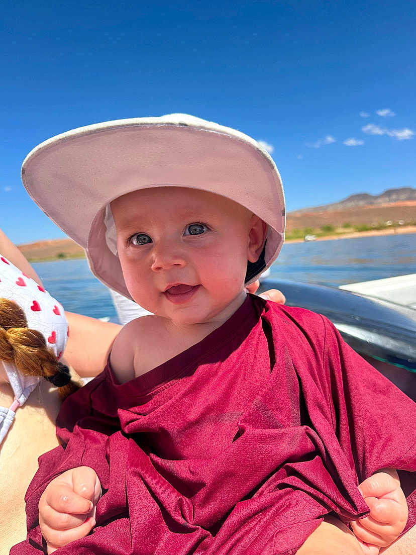 Octavia is registered to the contest to win money with this photo: baby, child, hat, smile, outdoor, water, sky, sunny, clothing, person, face, happy, nature, summer, portrait, boat, landscape, headwear, daylight, blue_sky