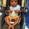 Nyjour joined the competition — help win amazing prizes! baby, child, car_seat, infant, blue_bib, white_shirt, tan_shorts, black_car_seat, curly_hair, barefoot, indoor, car_seat_strap, warning_labels, floor, blue_rug, cute, small_hands, small_feet, looking_up, seated
