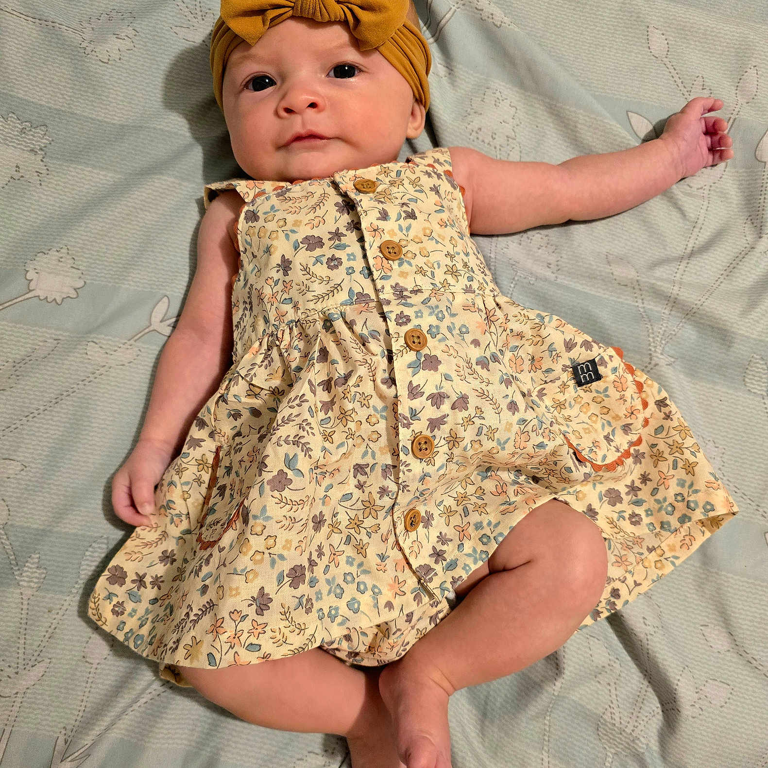 Percy joined the competition — help win amazing prizes! arm, baby, bedspread, bow, child, cute, dress, eyes, face, floral_pattern, foot, hand, headband, indoors, infant, leg, lying_down, portrait, skin, soft_lighting