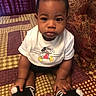 baby, child, infant, mickey_mouse, bib, socks, bedspread, patterned, indoor, portrait, person, cute, young, seated, small, black_hair, hands, feet, expression, clothing