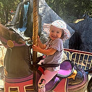 Skyla joined the competition — help win amazing prizes! child, girl, carousel, horse, amusement_park, waterfall, hat, smile, sunhat, leggings, outdoor, daylight, playful, fun, ride, nature, trees, purple, pink, sneakers
