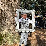 Léonardo participe au concours pour gagner de l'argent avec cette photo : child, boy, vintage_clothing, checkered_suit, bow_tie, suspenders, newsboy_cap, picture_frame, tree, outdoor, sunlight, shadow, people, food_station, event, grass, nature, portrait, smile, casual