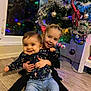 child, children, baby, smiling, hugging, christmas_tree, holiday, indoor, floor, decorations, ornaments, lights, festive, joyful, family, toddler, jeans, long_sleeve_shirt, window, home