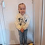 Chloé participe au concours pour gagner de l'argent avec cette photo : child, standing, indoor, door, white_shoes, hoodie, mickey_mouse, minnie_mouse, jeans, plush_toy, yellow_toy, floor, hands_clasped, braided_hair, casual_clothing, smiling, young_child, portrait, cute, shy