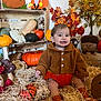 baby, pumpkin, autumn, fall_decor, hay, pinecone, orange_clothing, smiling, indoor, plush_toy, woodland_theme, decorative_leaves, child, seasonal, cute, sitting, cozy, orange_socks, festive, cute_face