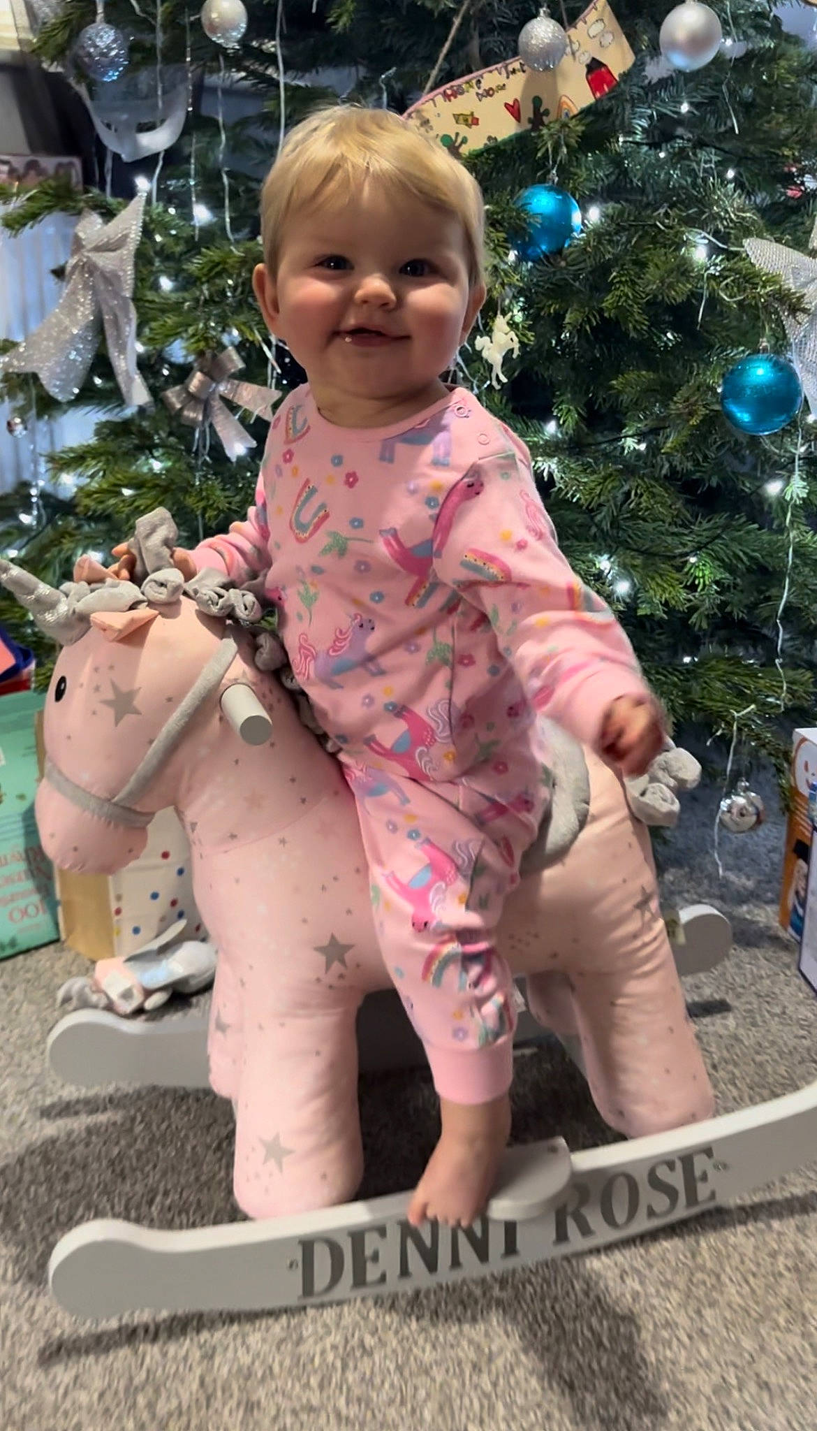 Denni-rose is registered to the contest to win money with this photo: baby, baby_toddler_clothing, barefoot, child, christmas_tree, event, foot, fun, grass, happy, holiday, human_leg, joy, people_in_nature, person, pink, sitting, smile, standing, thigh