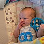 Noelle joined the competition — help win amazing prizes! baby, infant, toy, blue_toy, blanket, padded_seat, clothing, hand, face, expression, indoors, soft, comfort, child, cute, newborn, holding, colorful, pattern, resting