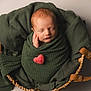 newborn, baby, swaddled, blanket, green_blanket, heart, pink_heart, basket, woven_basket, leather_handles, sleeping, peaceful, infant, cute, portrait, soft_lighting, cozy, tenderness, baby_wrapped, studio_photo