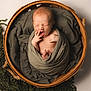 newborn, baby, yawning, wrapped, green_cloth, wooden_basket, blanket, knitted_fabric, infant, sleepy, cute, portrait, cozy, soft_lighting, studio_photo, small_hands, small_feet, peaceful, child, wrapped_baby