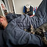 person, cat, blanket, bedroom, sleeping, nap, indoor, furniture, tabby_cat, rest, cozy, home, comfort, pillow, clothing, head, hair, doorway, bag, can