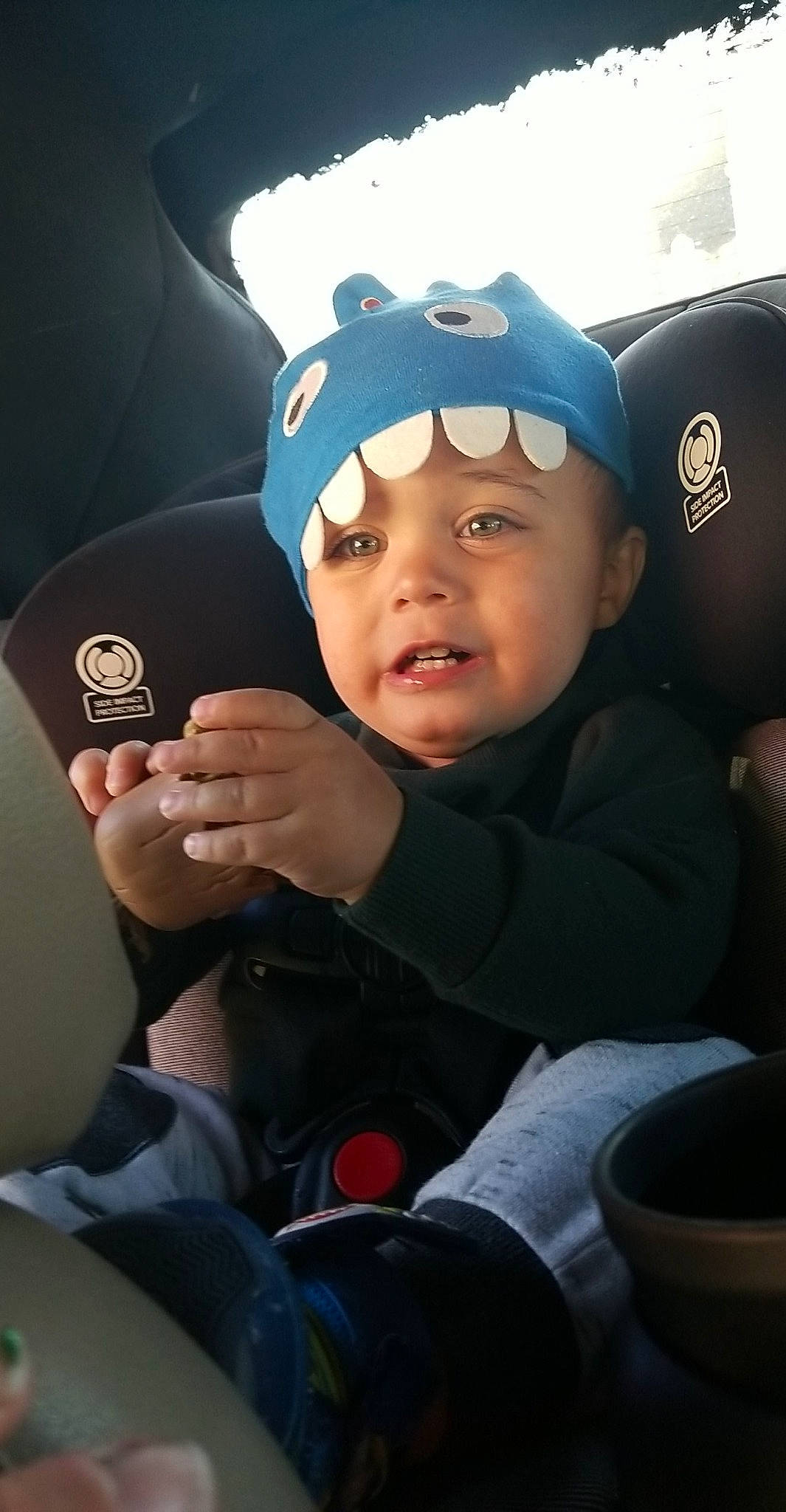 Xavier is registered to the contest to win money with this photo: baseball_cap, cap, car_seat, child, electric_blue, finger, fun, gesture, goggles, happy, hat, headwear, person, personal_protective_equipment, recreation, sitting, steering_wheel, t_shirt, thumb, toddler