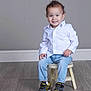 Dante is registered to the contest to win money with this photo: toddler, child, smile, white_shirt, blue_jeans, batman_sneakers, shoes, curly_hair, stool, wooden_floor, gray_wall, portrait, indoor, happy, casual_clothing, sitting, cute, young_child, fashion, studio