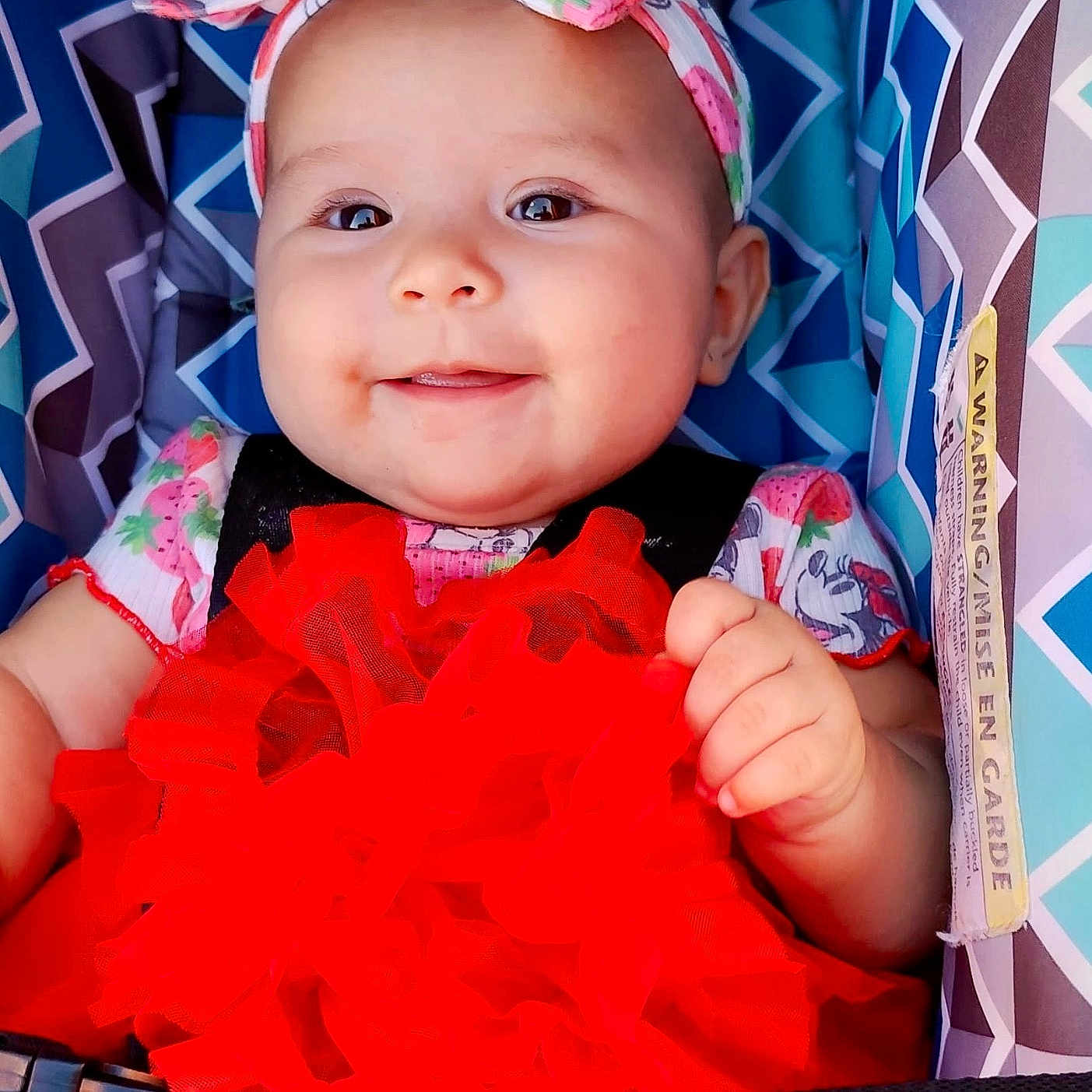 Sophie joined the competition — help win amazing prizes! baby, car_seat, child, closeup, clothing, colorful, cute, face, hand, happy, headband, indoors, infant, patterned_fabric, portrait, red_dress, seatbelt, sitting, smiling, young