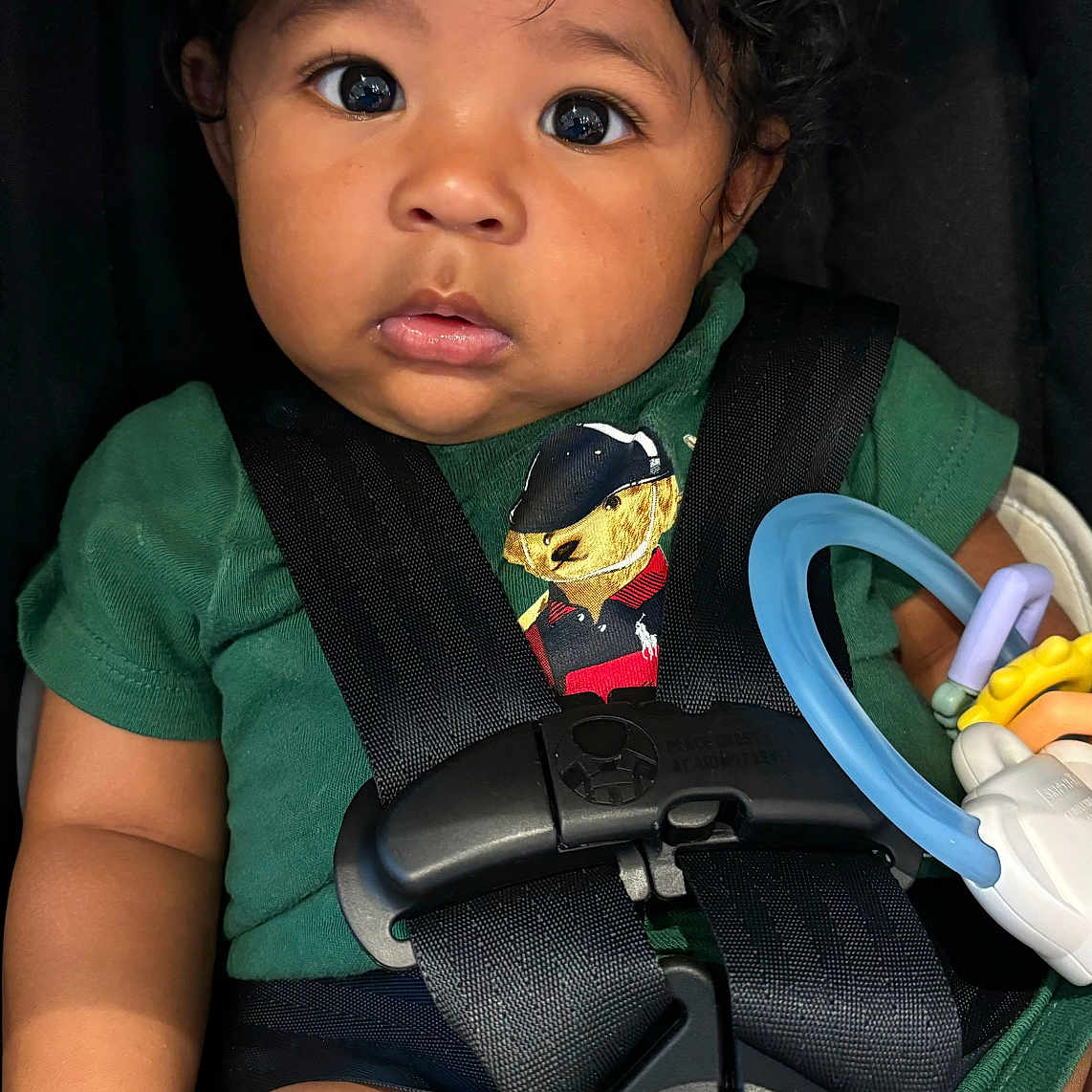 Yiannis joined the competition — help win amazing prizes! baby, black_straps, blue_ring, car_seat, child, chubby_legs, closeup, curly_hair, cute, expression, green_shirt, indoor, infant, person, portrait, safety_harness, teddy_bear, toy, wide_eyes, yellow_toy