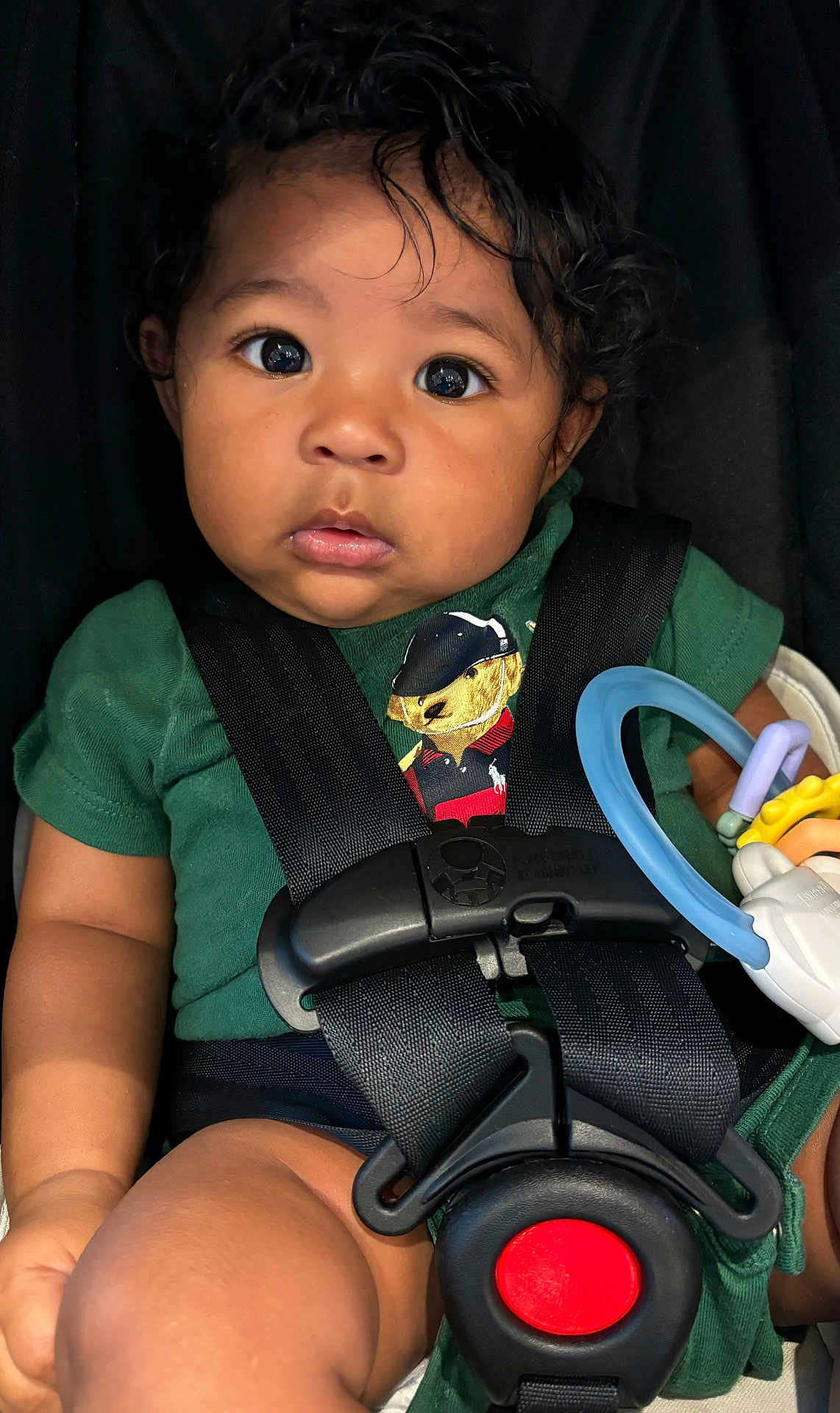 Yiannis joined the competition — help win amazing prizes! baby, black_straps, blue_ring, car_seat, child, chubby_legs, closeup, curly_hair, cute, expression, green_shirt, indoor, infant, person, portrait, safety_harness, teddy_bear, toy, wide_eyes, yellow_toy