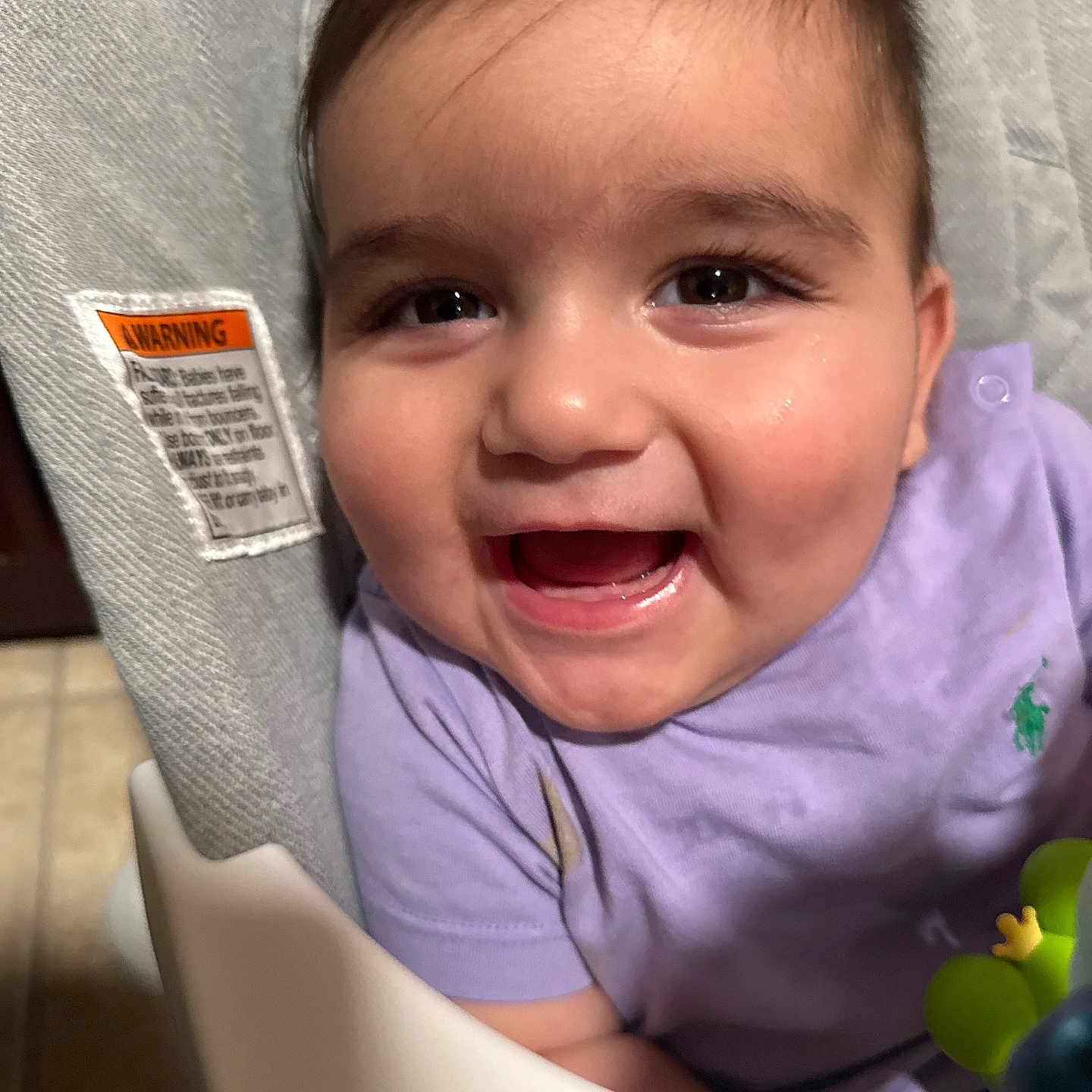 June is registered to the contest to win money with this photo: baby, child, smiling, happy, face, high_chair, purple_shirt, toy, indoor, close_up, cute, infant, portrait, person, young_child, cheerful, baby_clothing, skin, eyes, mouth