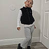 Antonella is registered to the contest to win money with this photo: child, portrait, standing, fashion, pose, hallway, indoors, door, wall, floor, wood_floor, clothing, vest, shirt, pants, shoes, black_shoes, short_hair, facial_expression, home