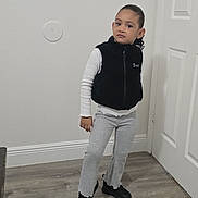 Antonella joined the competition — help win amazing prizes! child, portrait, standing, indoors, hallway, door, wood_floor, fashion, vest, sweatpants, long_sleeves, shoes, serious_expression, curly_hair, full_body, home, wall, baseboard, casual_clothing, photography