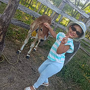 Antonella joined the competition — help win amazing prizes! child, cow, calf, outdoor, farm, animal, petting, sunglasses, sunhat, smiling, thumbs_up, striped_shirt, blue_pants, sandals, wooden_fence, woodland, sunlight, portrait, rural, happy
