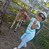 child, cow, calf, outdoor, farm, animal, petting, sunglasses, sunhat, smiling, thumbs_up, striped_shirt, blue_pants, sandals, wooden_fence, woodland, sunlight, portrait, rural, happy