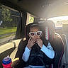 child, toddler, car, car_seat, sunglasses, sippy_cup, seatbelt,  안전, indoors, vehicle, passenger, sitting, fashion, sparkly, smiling, portrait, sunlight, window, family, travel