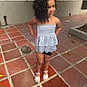 child, girl, toddler, curly_hair, smiling, portrait, outdoors, courtyard, pavement, tiles, dress, sandals, fashion, standing, hands_on_hips, person, face, hair, residential, daylight