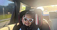 Antonella is registered to the contest to win money with this photo: child, toddler, car, car_seat, sunglasses, smiling, passenger, seatbelt, sippy_cup, vehicle_interior, travel, sunlight, window, road, outdoor, portrait, fashion,  안전, family, daylight