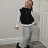 Antonella is registered to the contest to win money with this photo: child, smiling, portrait, full_body, indoors, hallway, door, wall, floor, wood_floor, standing, posing, playful, vest, sweater, pants, shoes, curly_hair, home, fashion