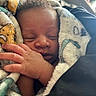 newborn, baby, sleeping, infant, face, hand, blanket, swaddled, portrait, close_up, indoors, cozy, peaceful, resting, skin, hair, parental_hand, soft_lighting, cuddled, car_seat