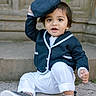 toddler, child, baby, blue_clothing, white_pants, navy_cap, sneakers, sitting, outdoor, stone_background, curly_hair, cute, playful, portrait, happy, person, casual, young_child, smiling, fashion