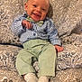 baby, child, smiling, sitting, bow_tie, blue_shirt, green_pants, socks, couch, floral_pattern, happy, cute, indoors, portrait, clothing, infant, young_child, comfort, home, person