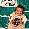 Ma'Kari joined the competition — help win amazing prizes! american_football, baby, casual_clothing, cheeks, child, cute, face_paint, football, green_background, handmade_sign, happy, indoor, jacket, playful, portrait, sign, sitting, smile, sporty, young_child