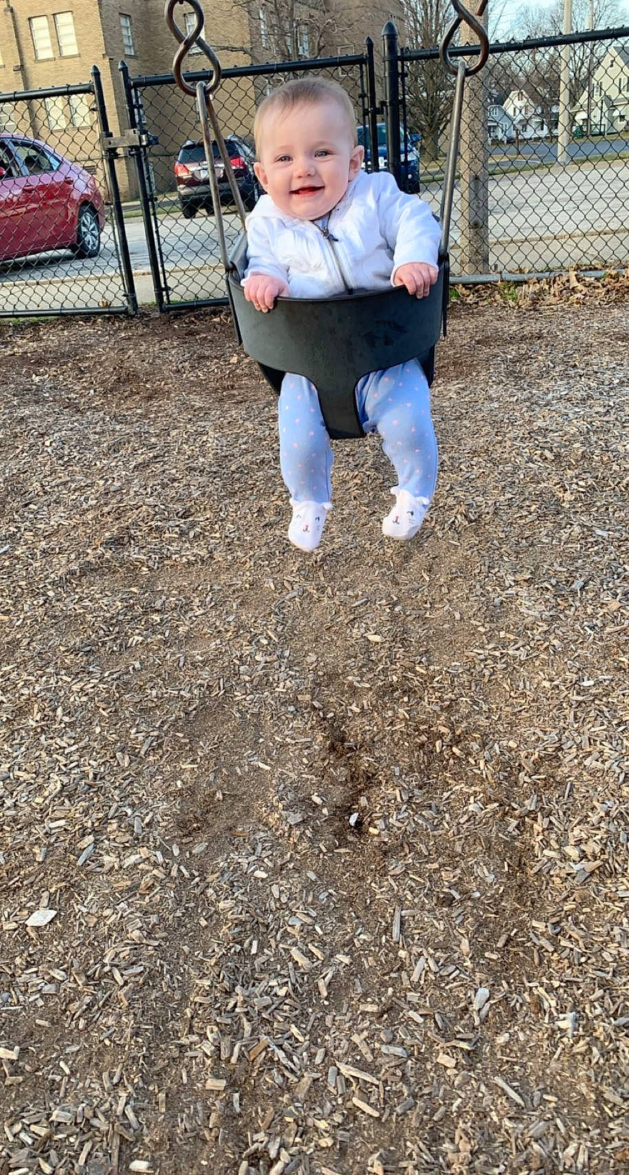 Melody is registered to the contest to win money with this photo: asphalt, baby, baby_toddler_clothing, city, compost, fence, garden, grass, joy, landscape, leisure, outdoor_play_equipment, people_in_nature, person, playground, public_space, recreation, smile, soil, swing