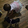 Tippy is registered to the contest to win money with this photo: baby, dog, floor, wooden_floor, crawling, dress, pink, white, black_dog, harness, indoor, shadow, child, pet, playing, cute, interaction, toddler, animal, home