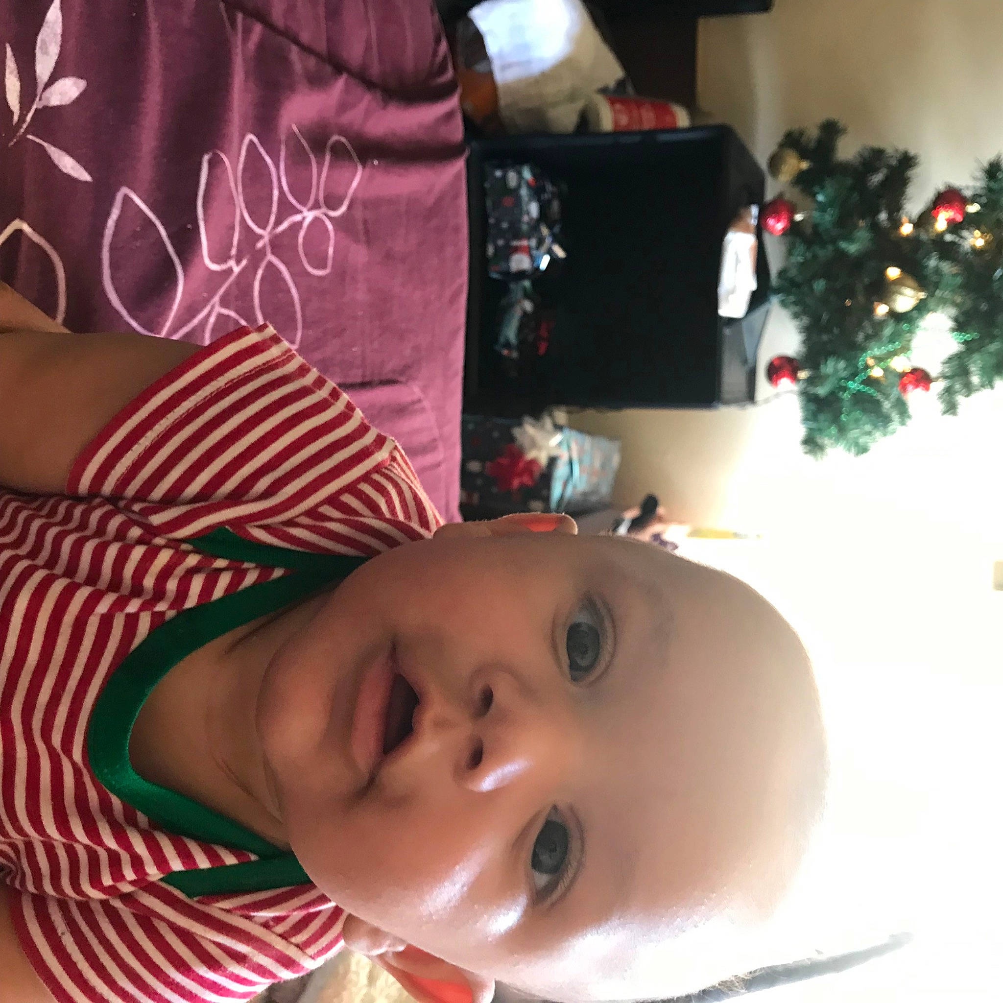 Jayden is registered to the contest to win money with this photo: baby, baby_toddler_clothing, cheek, child, christmas_ornament, christmas_tree, conifer, event, happy, holiday, mammal, nose, person, plant, red, room, skin, smile, toddler, tree