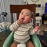 Anakin Lucas is registered to the contest to win money with this photo: baby, child, clock, clothing, curious, eyes, face, furniture, hand, high_chair, indoor, infant, living_room, portrait, sitting, smiling, striped_shirt, television, toys, window_blinds