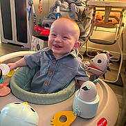 Ryker joined the competition — help win amazing prizes! baby, infant, smiling, sitting, activity_center, toy, play, button_shirt, face, eyes, mouth, drool, indoor, nursery, highchair, stroller, cabinet, blanket, furniture, happy