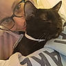 person, cat, black_cat, glasses, collar, sleeping_cat, close_up, indoor, cozy, hug, smile, face, eyewear, apparel, cuddle, pet, comfort, portrait, resting, warmth