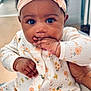 baby, infant, child, headband, hand, fingers, onesie, floral_pattern, indoor, curly_hair, cute, sitting, portrait, skin, large_eyes, cozy, holding, person, young, apparel
