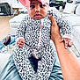 Logan is registered to the contest to win money with this photo: baby, child, infant, onesie, leopard_print, headband, pink_bow, hand, living_room, couch, blanket, carpet, television, plant, furniture, person, indoor, portrait, cute, seated